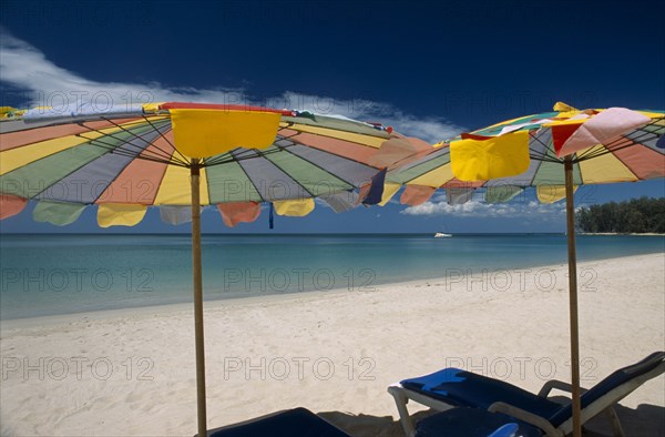 THAILAND, North Phuket, Naiyang Beach, "Two multi coloured parasols and sun loungers on the sandy beach, boat in the distance."
