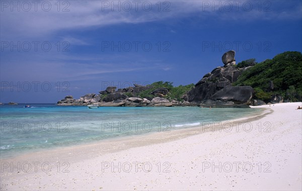 THAILAND, Koh Similan , Sail Rock, View along the sandy beach with people and boats near the rocky coast line.