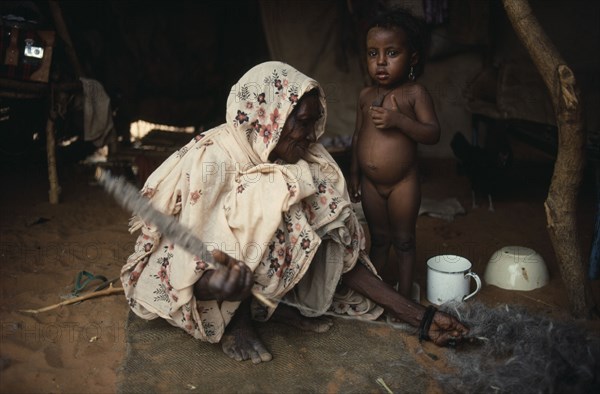 SUDAN, North Kordofan, Work, Kababish nomad woman spinning wool inside hut with little girl standing beside her.