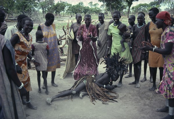 SUDAN, Tribal People, Dinka Binzar or witch doctor wearing head-dress of feathers on ground in trance surrounded by tribeswomen.