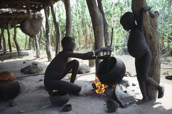 SUDAN, Tribal People, Dinka children cooking over open fire beneath house raised above ground level .