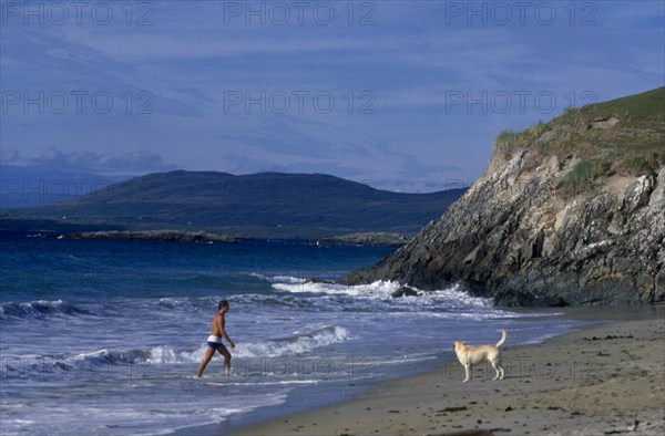 IRELAND, County Galway, Galway, Beach with man walking out of surf towards a dog on the sand