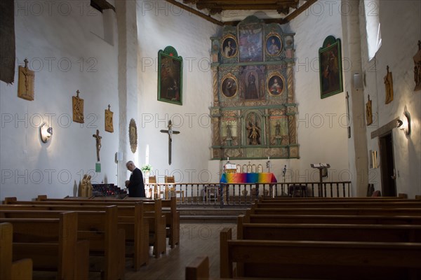 USA, New Mexico, Santa Fe, The altar and nave of the San Miguel Mission church with a priest lighting candles beside the left wall