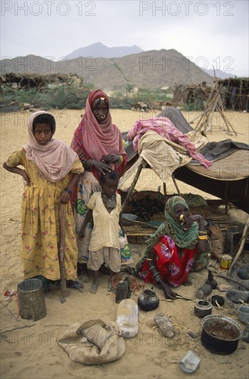 SUDAN, North East, Gadem Gafriet Camp, "Beni Amer nomad refugee women and children outside small, makeshift tent in desert camp."