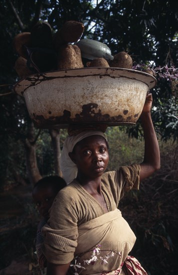 GHANA, People, Women, Portrait of young woman carrying bowl of yams on her head and baby in sling on her back.