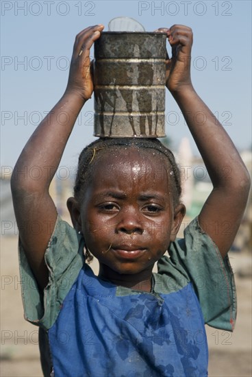 GUINEA, Kissidougou Camp, Portrait of Sierra Leonean refugee girl carrying can of water on her head in camp for displaced people.