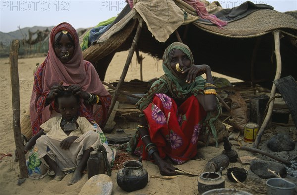 SUDAN, North East, Gadem Gafriet Camp, Beja nomad Beni Amer tribeswomen and child outside tent in refugee settlement.