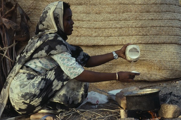 SUDAN, Red Sea Hills Province, Beja nomad woman cooking mededa gruel made from sorghum over open fire.