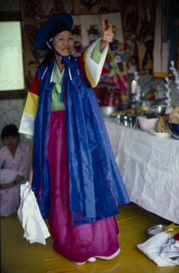 SOUTH KOREA, Religion, Shamanism, Female Shaman with arm raised in air at a funeral wearing colourful clothing.