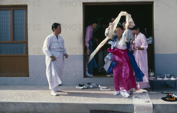 SOUTH KOREA, Religion, Shamanism, Female Shaman in a trance at a wedding waving cloth above her head with people looking on