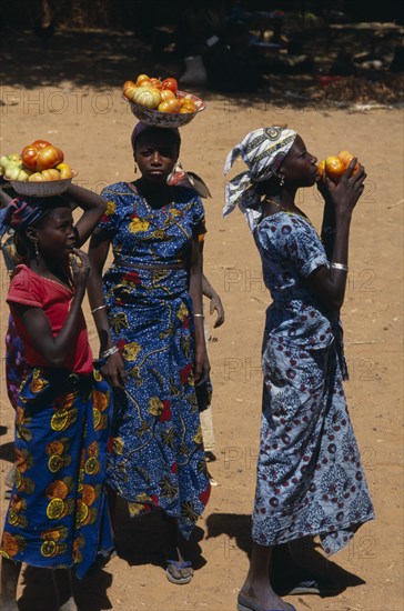 NIGER, People, Girls, Girls wearing brightly coloured dresses selling tomatoes carried in bowls on their heads.