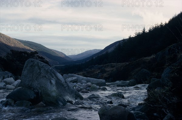 IRELAND, Co. Wicklow, Glenmalure Valley, Wicklow Mountains in winter with rocks in river in the foreground under fine covering of snow.