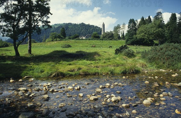 IRELAND, Co. Wicklow, Glendalough, Ruins of St Kevin’s monastery  dating from the Sixth Century set in rural landscape with stream in the foreground.