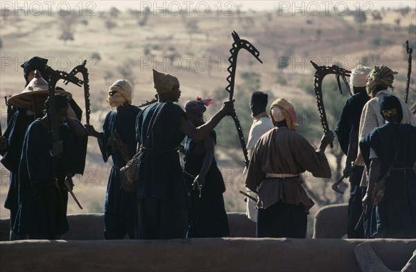 MALI, Ceremony, Dogon men carrying carved wooden staffs symbolic of ancient Dogon society performing rooftop dance.