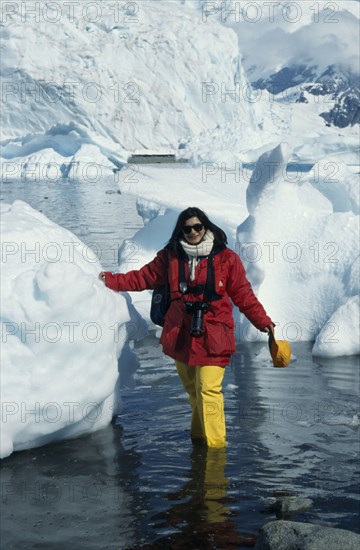 ANTARCTICA, Paradise Harbour, A tourist with camera stands in the water next to icebergs in Waterboat  Point.