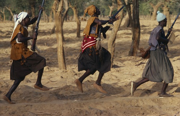 MALI, Ceremony, Dogon funeral dance.  Dancers carrying rifles leaping in line.