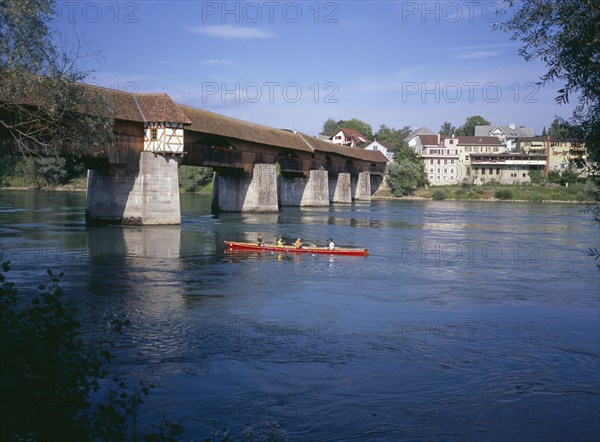GERMANY, Baden Wurttemberg, Covered wooden bridge over the Rhine which links Badsackingen with the Stein in Switzerland. People in row boat.