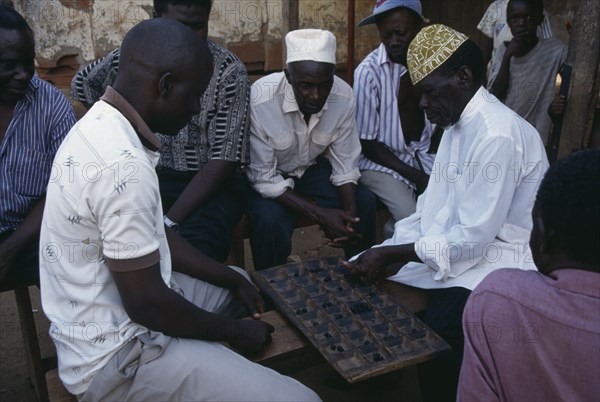 UGANDA, Kampala, Group of men playing board game of mweso in the street.  A type of mancala also known as omweso or mbao using an 8x4 board.
