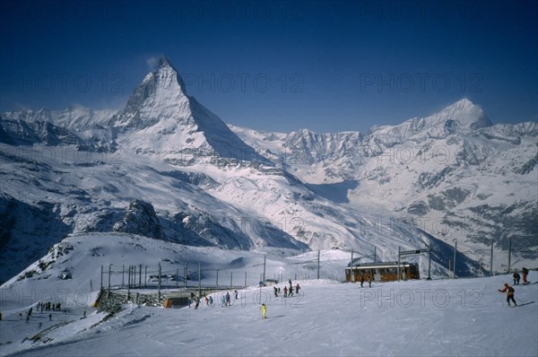 SWITZERLAND, Valais, Zermatt, Skiers on slopes in foreground with Matterhorn behind.