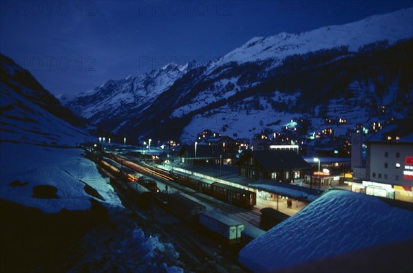 SWITZERLAND, Landscape, Ski resort chalets and train station in snow covered mountain landscape at night with lights from windows and platform.