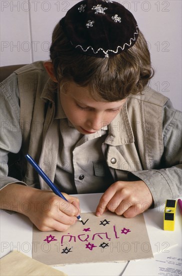 ENGLAND, Religion, Judaism, Boy at Sunday school wearing a kippah and making a card with Hebrew lettering.