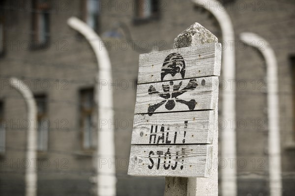 POLAND, Oswiecim, Auschwitz, Detail of a sign in the concentration camp. Black scull and crossbones on white painted wood with a warning written underneath.