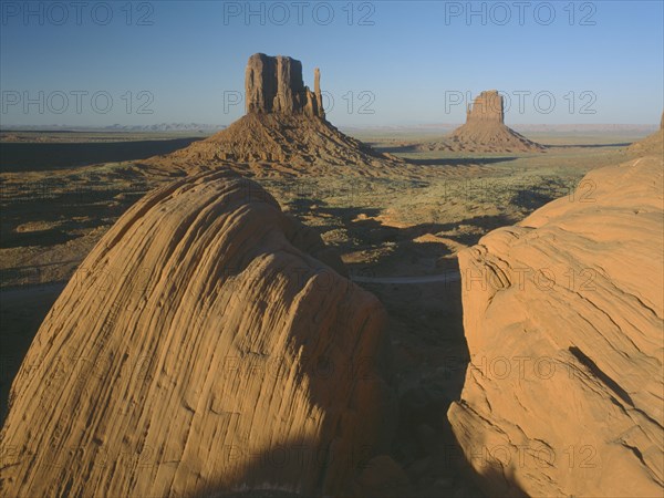 USA, Arizona, Monument Valley, Rock formations with a golden sunset glow on the valley with rocks in the foreground