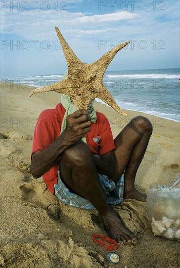 INDIA, Tamil Nadu, Auroville Beach, An elderly sea-shell seller returns to work 5 weeks after the Indian Ocean Tsunami hit Auroville Beach on December 26th 2004.