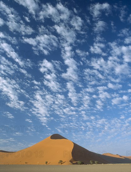 NAMIBIA, Namib Desert, Sossusvlei, Sand dune with dramatic clouds scattered in a blue sky above seen in early morning light