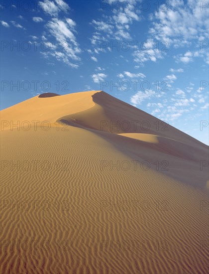 NAMIBIA, Namib Desert, Sossusvlei, Sand dune with dramatic clouds scattered in a blue sky above seen in early morning light