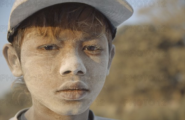 BURMA, Mandalay, "Portrait of a young boy worker in Mandalay dock with cement dust on his face, wearing a baseball cap. Banks of the Irrawaddy"