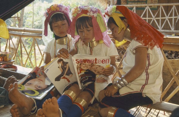 THAILAND, Chiang Rai, "Portrait of young Paduang girls in costume, reading a magazine, long neck, metal rings."