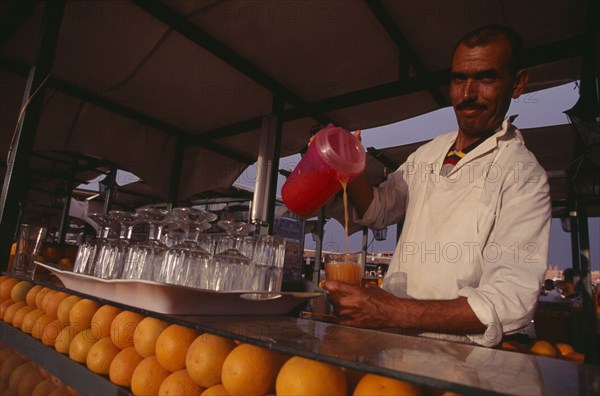 MOROCCO, Marrakech, Dejemma el Fna. A man pouring a glass of orange juice. Rows of oranges and glasses on the bar.