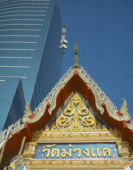 THAILAND , Bangkok, The peak of the roof of the Wat Muang Khae Temple with the Communications Authority of Thailand building behind.