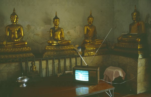 THAILAND, Media, Television, Thai boxing on television inside a monastery in front of seated Buddha figures.