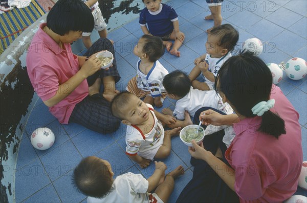 THAILAND, North, Chiang Mai, Staff feeding young children in Vienping Orphanage.