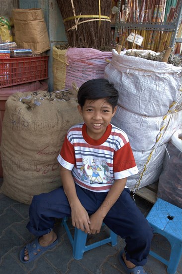 VIETNAM, South, Ho Chi Minh City, A young boy sitting next to sacks of dried herbs. Son of the owner of the Chinese herbal shop