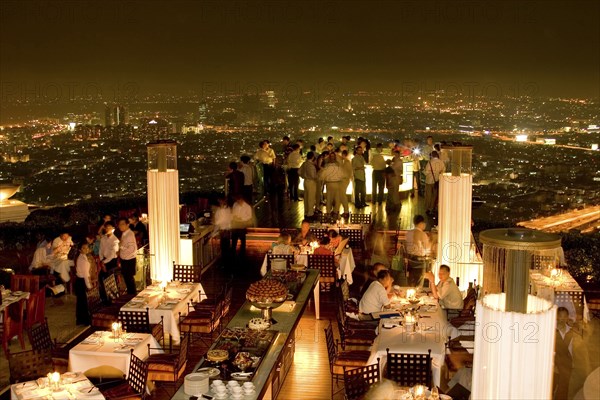 THAILAND, Bangkok, Sorocco Restaurant. People dining at tables with the Bangkok Skyline in the background.