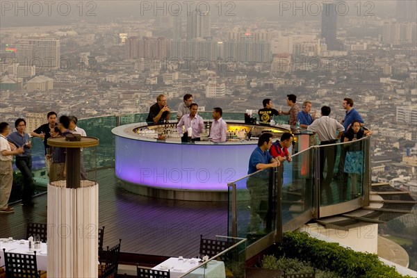 THAILAND, Bangkok, Sorocco Restaurant. People standing next to a lit up bar and looking over balcony surrounded by the Bangkok Skyline