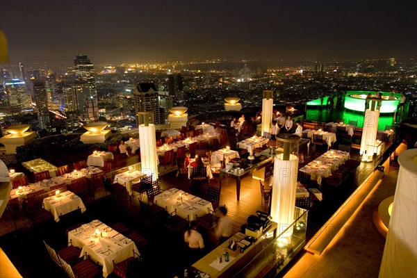 THAILAND, Bangkok, Sorocco Restaurant. View over people dining at tables lit up with light displays and the Bangkok Skyline in the background.