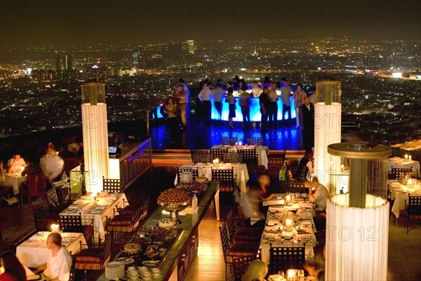 THAILAND, Bangkok, Sorocco Restaurant. View over people dining at tables lit up with light displays and the Bangkok Skyline in the background.