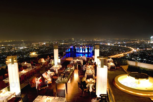 THAILAND, Bangkok, Sorocco Restaurant. View over people dining at tables lit up with light displays and the Bangkok Skyline in the background.