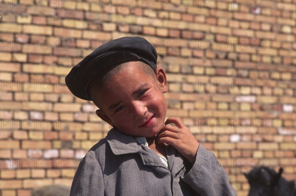 CHINA, Xinjiang Province, Kashgar, Portrait of young Tajik boy standing in front of brick wall