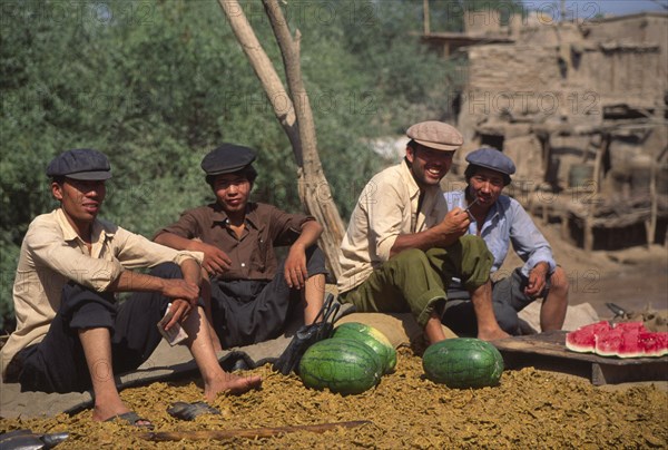 CHINA, Xinjiang Province, Kashgar, Group of Tajik men sat on ground eating water melon