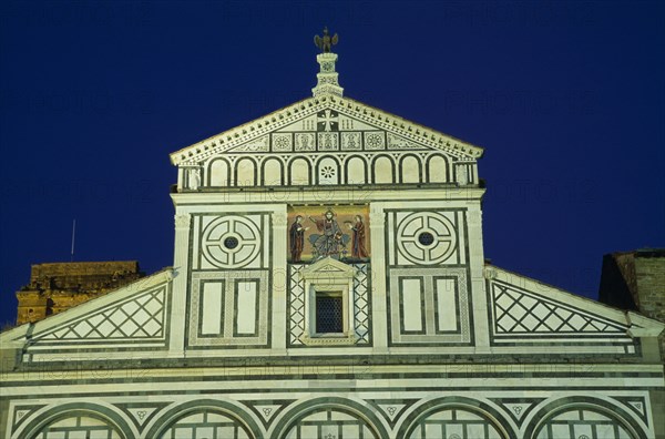 ITALY, Tuscany, Florence, San Miniato al Monte Romanesque church begun in 1018.   Exterior facade with geometric marble patterning and steps to entrance illuminated at night.