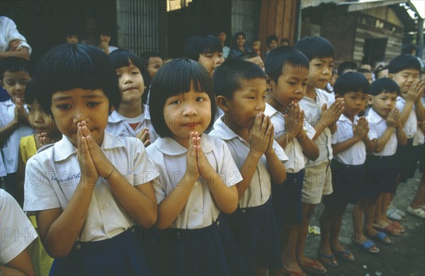 THAILAND, Tap Gaen, Line of school children giving traditional Thai greeting or wai with palms together and fingers extended.
