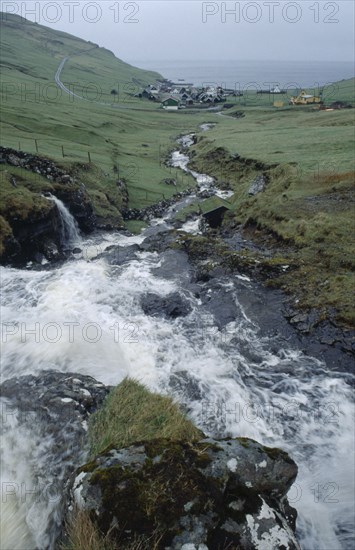 DENMARK, Faeroe Islands, River Gazadalla, Fast flowing rocky river with village and coastline beyond.