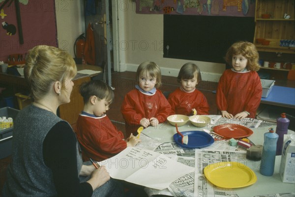 EDUCATION, School, Nursery, Nursery School children with teacher gathered around table taking part in art class.