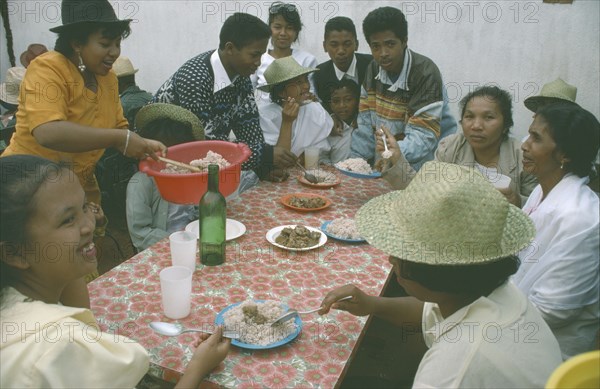 MADAGASCAR, Antananarivo, Large group of people having a meal of meat and rice.  Rice is a staple food and eaten at all meal times.