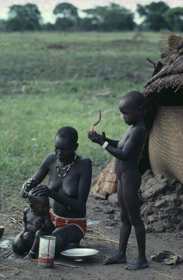 SUDAN, South, Dinka mother washing her baby with older daughter standing beside her.